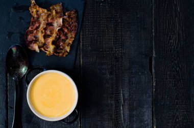 Siyah arka planda kızarmış pastırma ile kabak püresi çorbası.