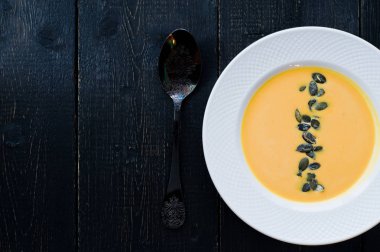 Siyah bir arka plan üzerinde beyaz bir tabakta tohumları ile kabak çorbası.