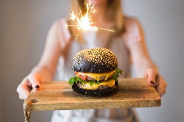 Kız şef elinde siyah cheesburgers ile ahşap kesme Kurulu tutar