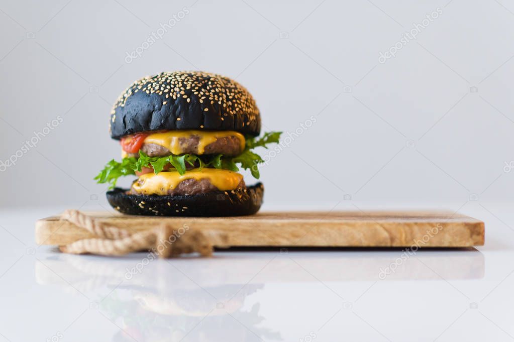 Black Burger on wooden chopping Board, grey background.