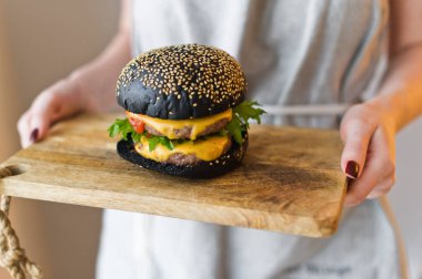 Kız şef elinde siyah cheesburgers ile ahşap kesme Kurulu tutar