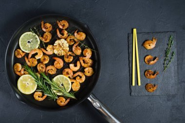 Sarı çubuklar ile siyah bir arka plan üzerinde bir tavada kızarmış kral karides.