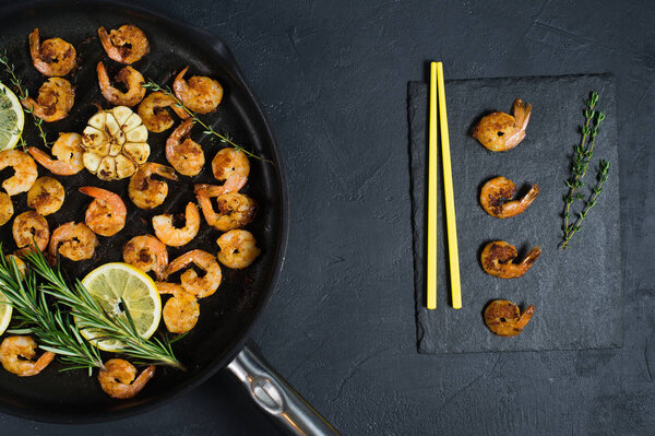 Fried king prawns in a frying pan on a black background with yellow chopsticks.