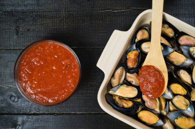 Siyah arka planda domates salçası ile çiğ midye, pişirme.