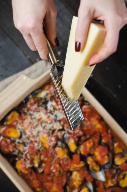 Şef domates soslu midye üzerine peynir sürüyor.