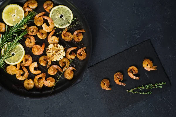 Fried king prawns in a frying pan on a black background.