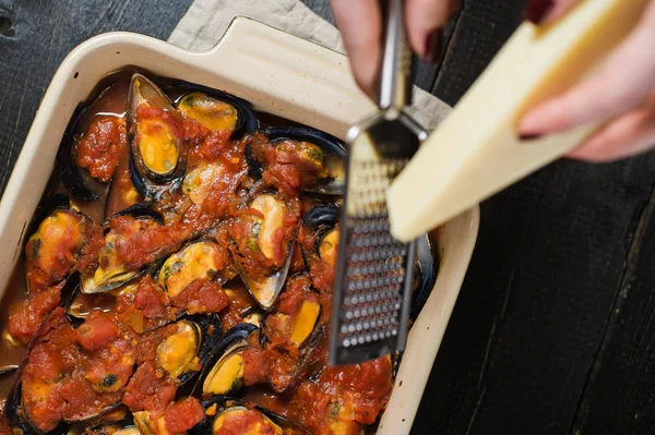 Chef rubs cheese on the mussels in tomato sauce. — Stock Photo, Image