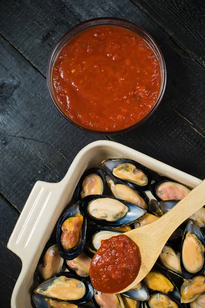 Siyah arka planda domates salçası ile çiğ midye, pişirme.