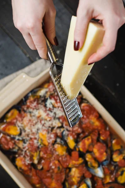 Şef domates soslu midye üzerine peynir sürüyor.