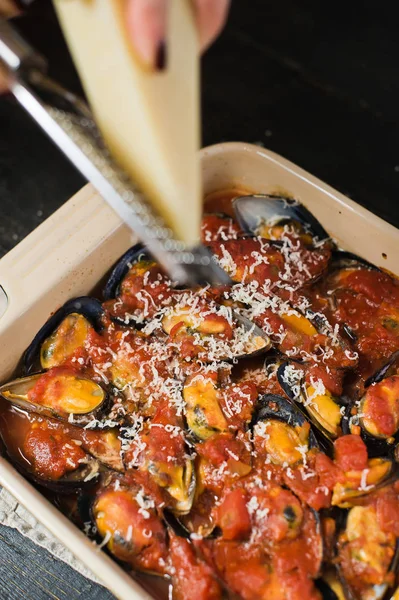 Şef domates soslu midye üzerine peynir sürüyor.