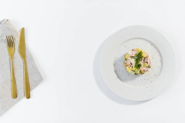 Salade russe sur une assiette blanche avec un couteau doré et une fourchette sur fond blanc . — Photo