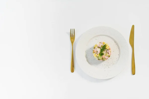 Orosz saláta fehér lemezen, arany késsel és villával, fehér alapon. — Stock Fotó