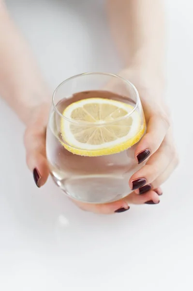 Manos sosteniendo un vaso de agua clara con limón . — Foto de Stock