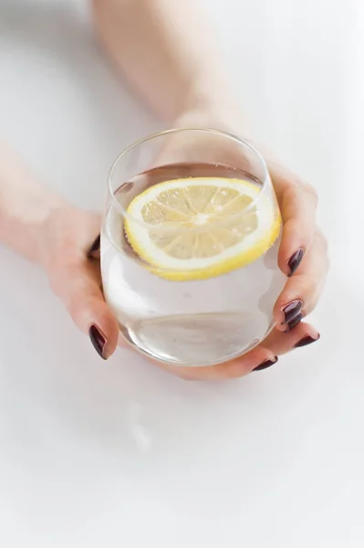 Manos sosteniendo un vaso de agua clara con limón . — Foto de Stock