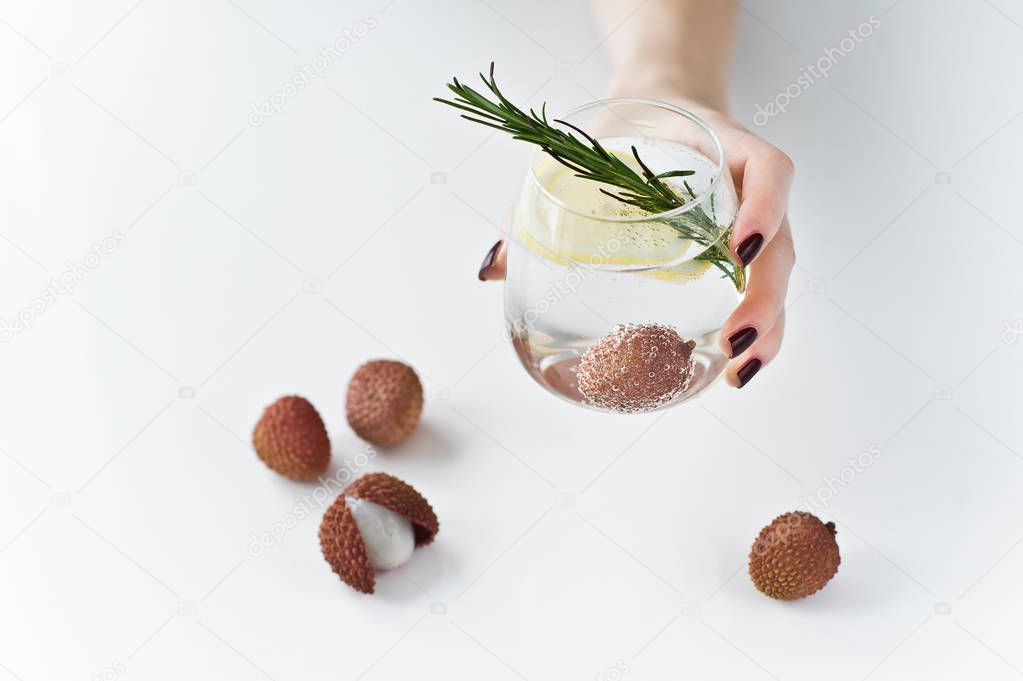 hand holding a glass of clear water with lemon, rosemary, lychee