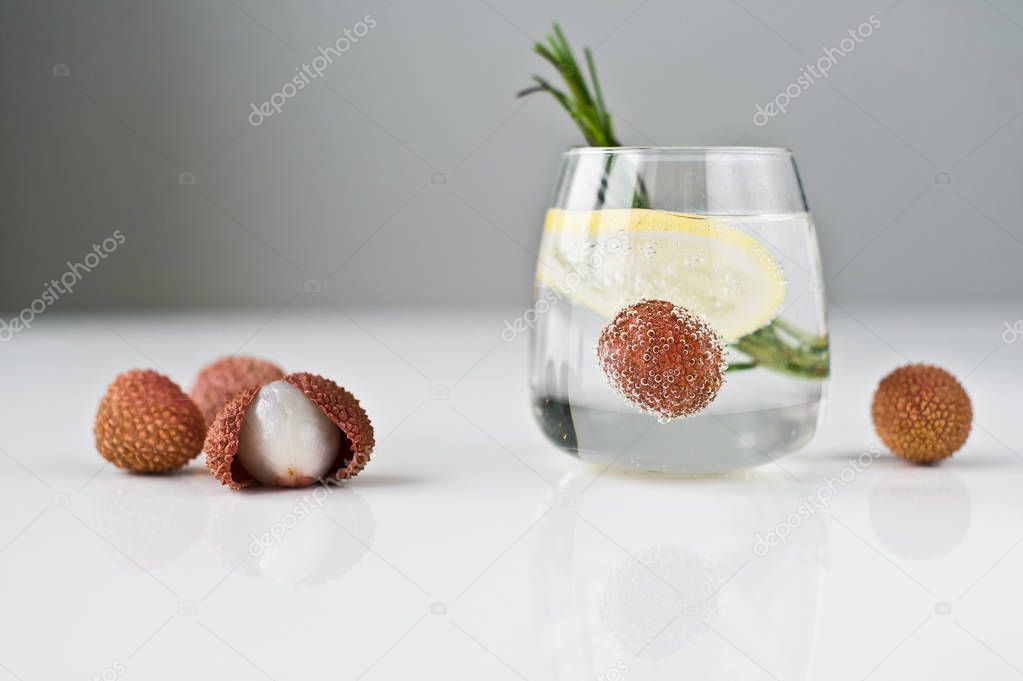 glass of clear water with lemon, rosemary, lychee.