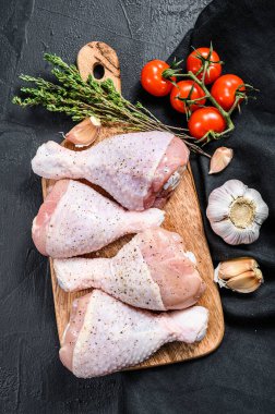 Tahta kesme tahtasına baharat ve sebze konmuş çiğ tavuk budu. Siyah arka plan. Üst görünüm.