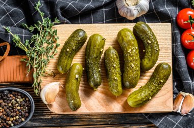 Salamura edilmiş salatalık turşusu ve kesme tahtasında baharatlar. Siyah arka plan. Üst görünüm.