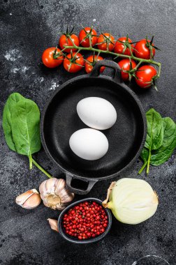Kızarmış ya da haşlanmış yumurta ile kahvaltı hazırlama kavramı. Yumurta, soğan, sarımsak, domates, biber, ıspanak. Siyah arka plan. Üst görünüm.