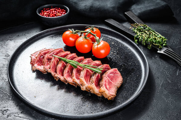 Sliced Grilled Top Blade steak on a plate. Organic beef meat. Black background. Top view.