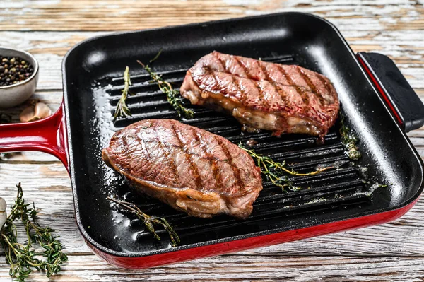 Grilled meat Top Blade steaks in a frying pan. Gray background. Top view.
