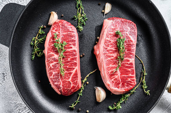 Raw top-blade steak in a pan. Gray background. Top view.