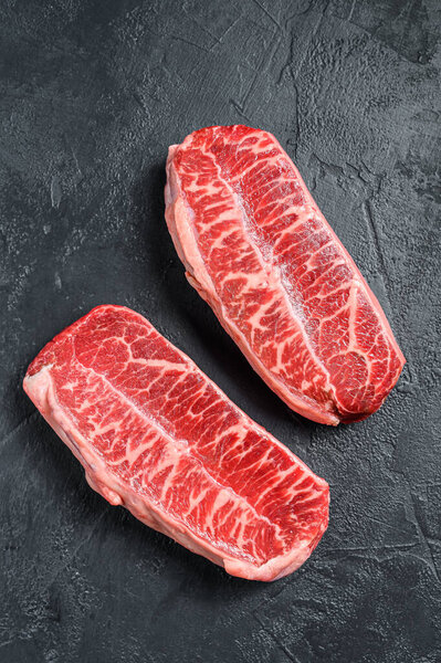 Raw top blade steak dry-aged. Black background. Top view.