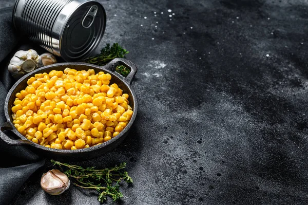 Canned corn in a pan. Canned food. Black background. Top view. Copy space.