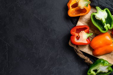 Yarısı dilimlenmiş portakal, yeşil ve kırmızı dolma biber. Siyah arka plan. Üst Manzara. Metin için boşluk.