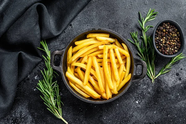 French fries in a pan, fried potatoes. Black background. Top view.