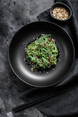 Çubuklu bir tabakta susam tohumlu yosun salatası. Siyah arka plan. Üst görünüm.