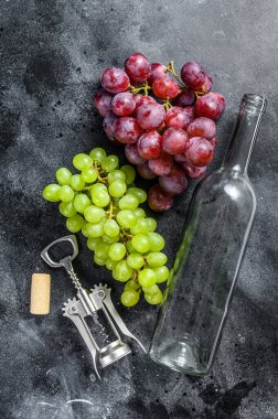 Bir dal yeşil ve kırmızı üzüm, bir şişe, bir tirbuşon ve bir mantar. Şarap yapma kavramı. Siyah arka plan. Üst görünüm.