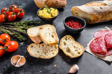 Bagetli sandviç malzemeleri - jambon, salam, peynir, tereyağı, domates. Siyah arka plan. en üstteki görünüm.