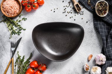 Taze çiğ sebze ve sebzelerin ortasında siyah boş bir tabak. Sağlıklı, temiz yemek, vejetaryen, diyet yemek konsepti. Beyaz arka plan. Üst Manzara. Boşluğu kopyala.