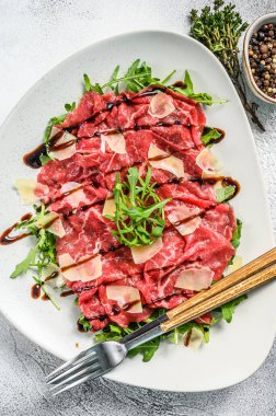 Parmesan peyniri ve roka ile beyaz tabakta sığır eti carpaccio. Gri arka plan. Üst görünüm