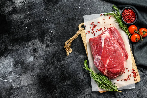 Raw brisket beef cut on a wooden cutting board. Black Angus beef. Black background. Top view. Copy space.