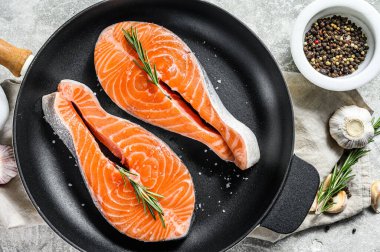 Kızartma tavasında çiğ somon bifteği. Sağlıklı deniz ürünleri. Gri arka plan. Üst görünüm.