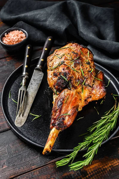Baked lamb, sheep leg with rosemary. Dark wooden background. Top view.
