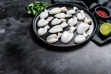 Biberiye ve maydanozlu çiğ mürekkep balığı. Siyah arka plan. Üst Manzara. Boşluğu kopyala.