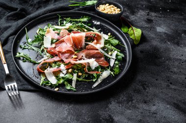 Parmalı salata, jambon, roka ve parmesan peyniri. Siyah arkaplan, üst görünüm, metin için boşluk.