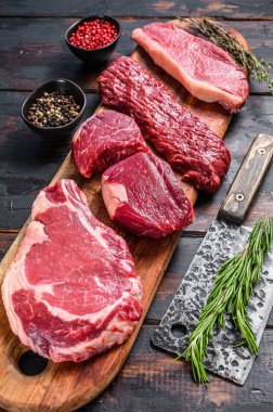 Assortment of raw beef steaks Tenderloin fillet mignon, ribeye, Striploin or new york, skirt, machete. Wooden dark background. Top view. clipart