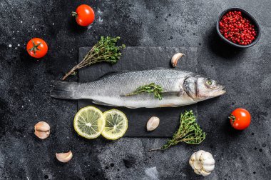 Siyah tabakta taze deniz levreği, şifalı otlar ve limon. Siyah arka plan. Üst görünüm