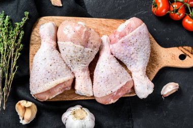 Tahta kesme tahtasına baharat ve sebze konmuş çiğ tavuk budu. Siyah arka plan. Üst görünüm.