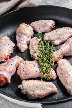 Baharatlı tavuk kanatları ve tavada pişmeye hazır bitkiler. Gri arka plan. Üst görünüm.