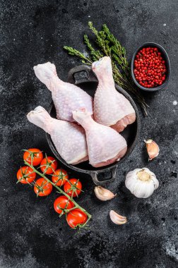 Taze tavuk budu, kızartma tavasında pişirmek için malzemeli bacaklar. Organik kümes hayvanları. Siyah arka plan. Üst görünüm.