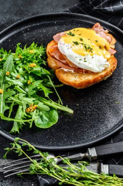Pastırmalı Brioche sandviç, Benedict usulü yumurta ve Hollandaise sosu. Arugula salatalı garnitür. Siyah arka plan. Üst görünüm.