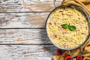 Krema soslu orzo makarna, pastırma ve fesleğen. Hazır risoni. Beyaz ahşap arka plan. Üst Manzara. Boşluğu kopyala.