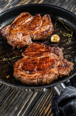 Chuck 'ın tavada pişirdiği ızgara mermer biftek. Karanlık arka plan. Üst görünüm.