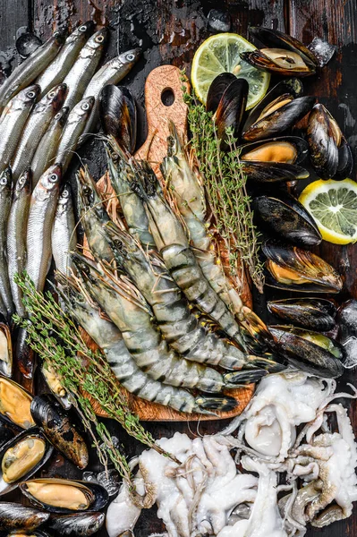 Raw seafood tiger prawns, shrimps, blue mussels, octopuses, sardines, smelt. Black wooden background. Top view.