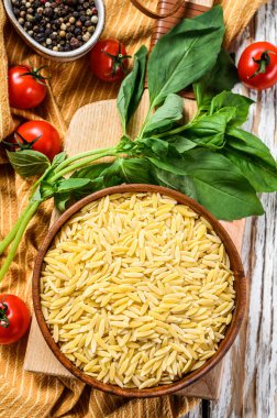 Bir kase çiğ Orzo makarna, fesleğen yaprağı, domates ve sarımsaklı. Beyaz arka plan. Üst görünüm.